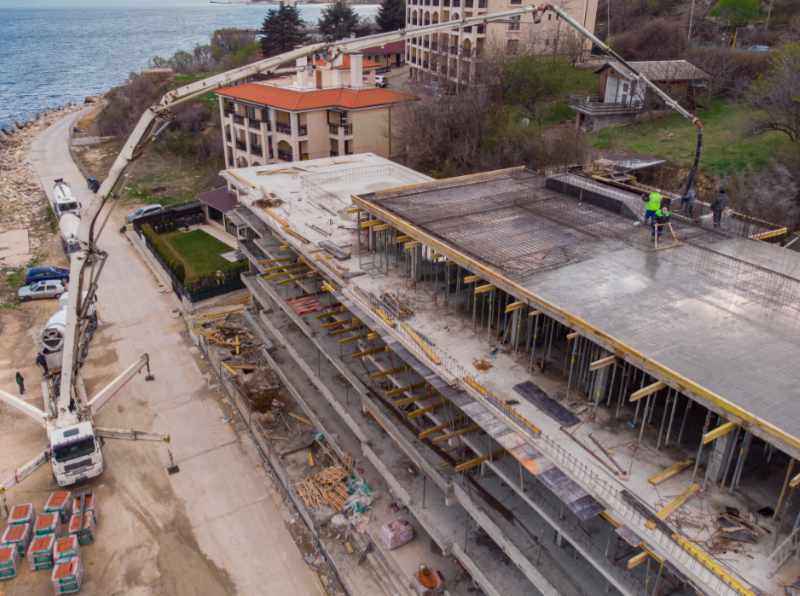 Pouring concrete cement on the roof of residential building under construction using a concrete pump truck machine with high boom to supply the mixture to the upper floors. Aerial drone view.